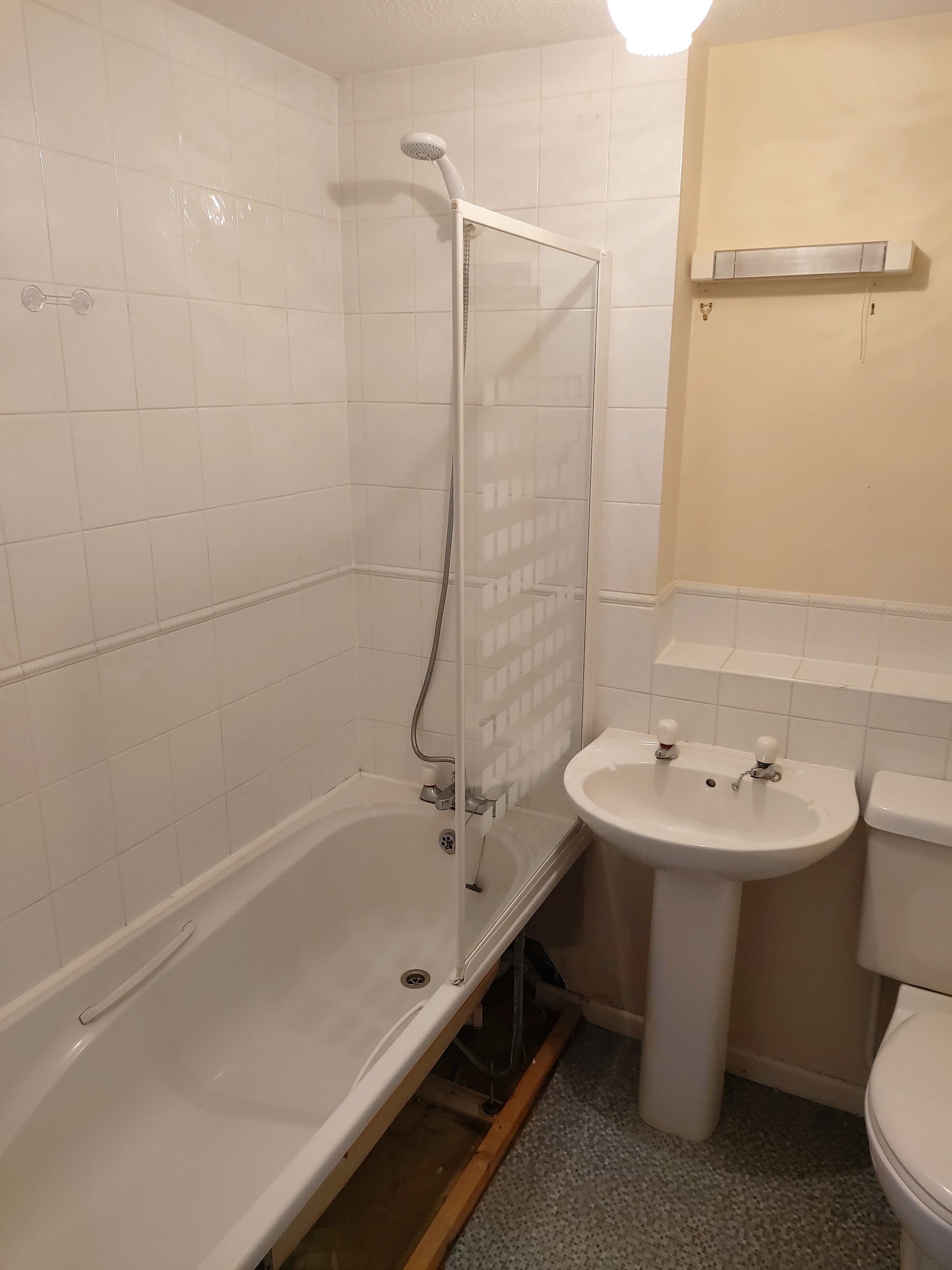 An old white-tiled bathroom with a bath, shower screen and pedestal basin before the work