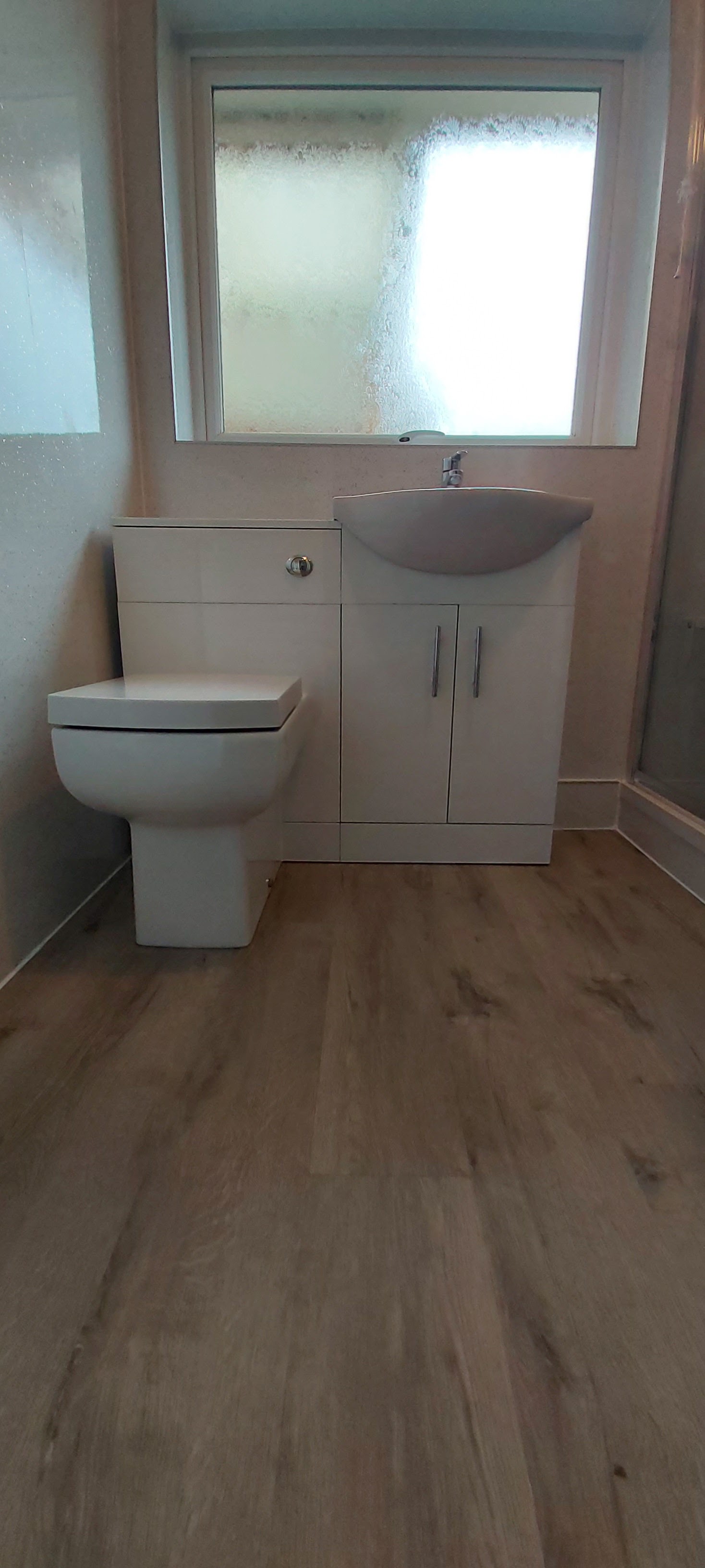 The same room finished with a white vanity unit, a modern toilet and a wood-effect floor