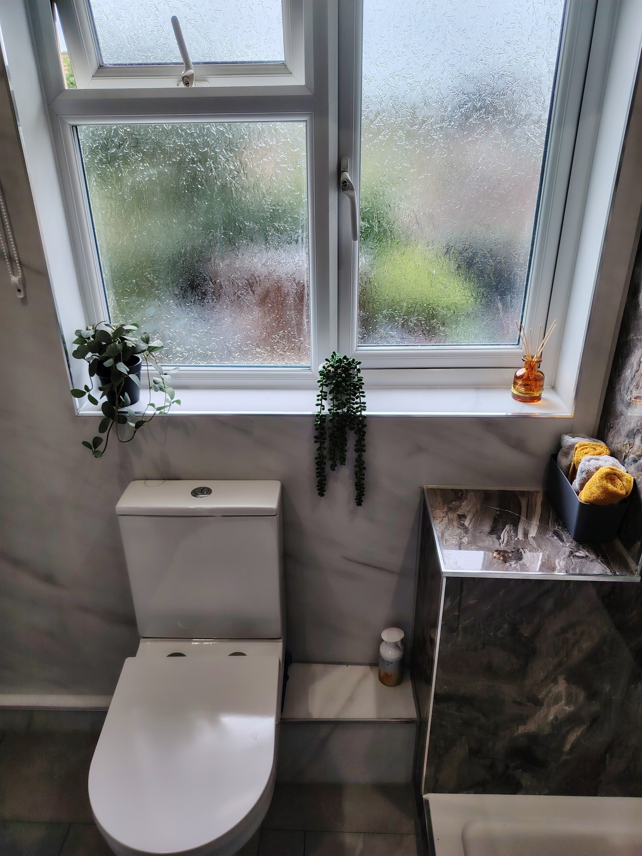 A rimless toilet and vanity unit under a frosted window, with marble-effect panelling