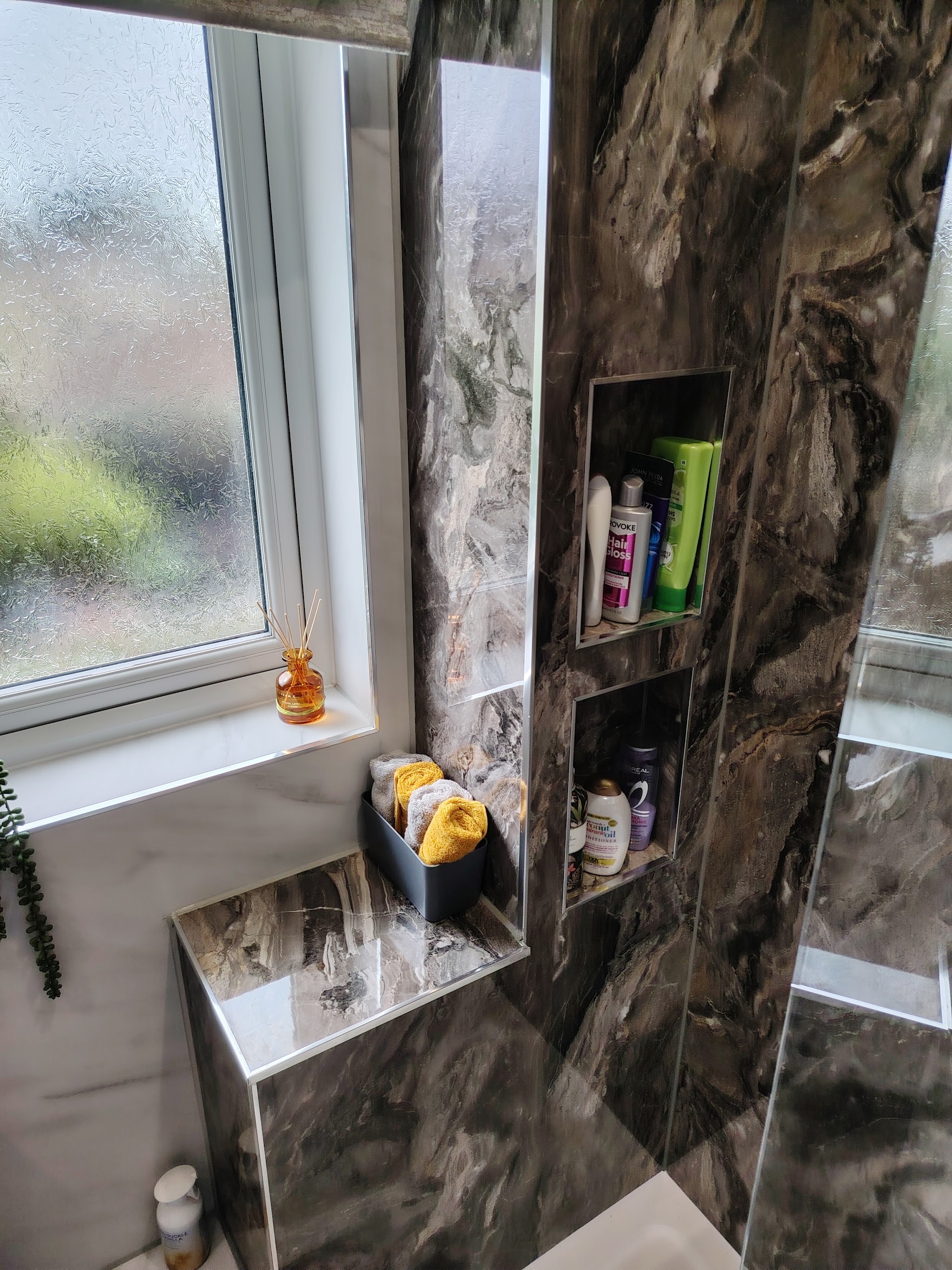 A shower finished in marble-effect wall panels with two recessed shelves