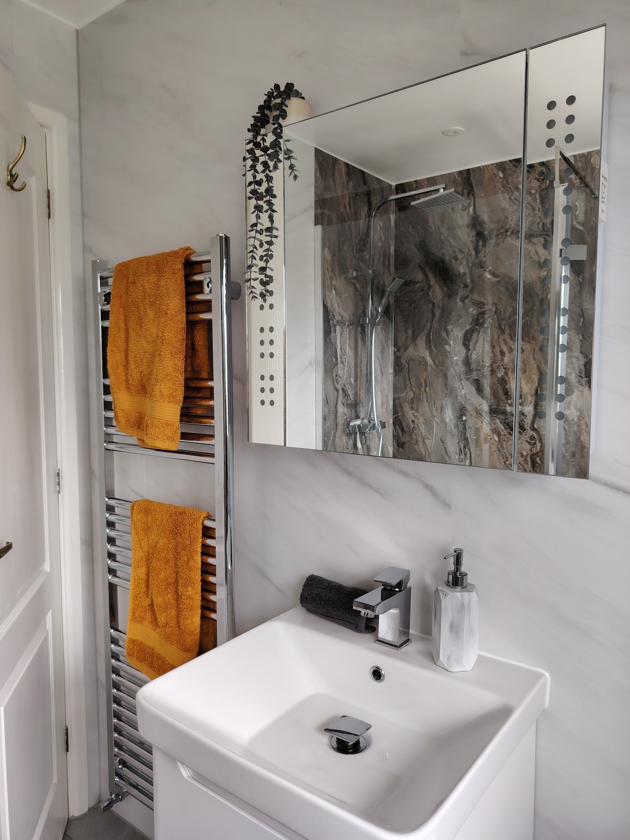 A white vanity basin with a mirror cabinet and a chrome heated towel rail